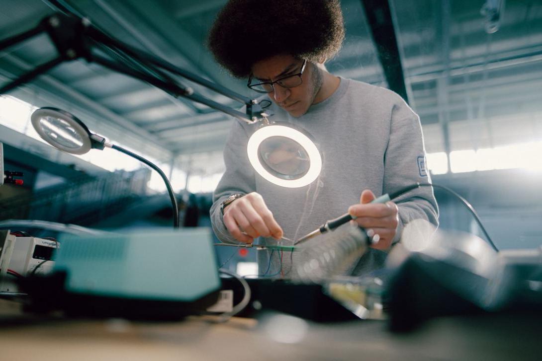 A Kettering electrical engineering student looks through a magnifying glass to couple electrical wires