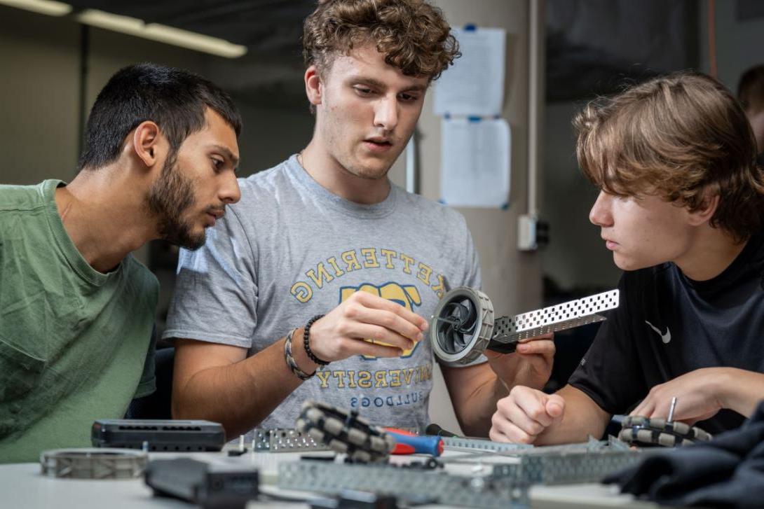 Three Kettering industrial engineering students work on machine parts